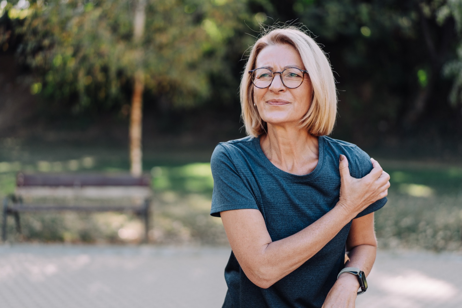 Woman holding her shoulder in pain outdoors, before seeing a frozen shoulder specialist