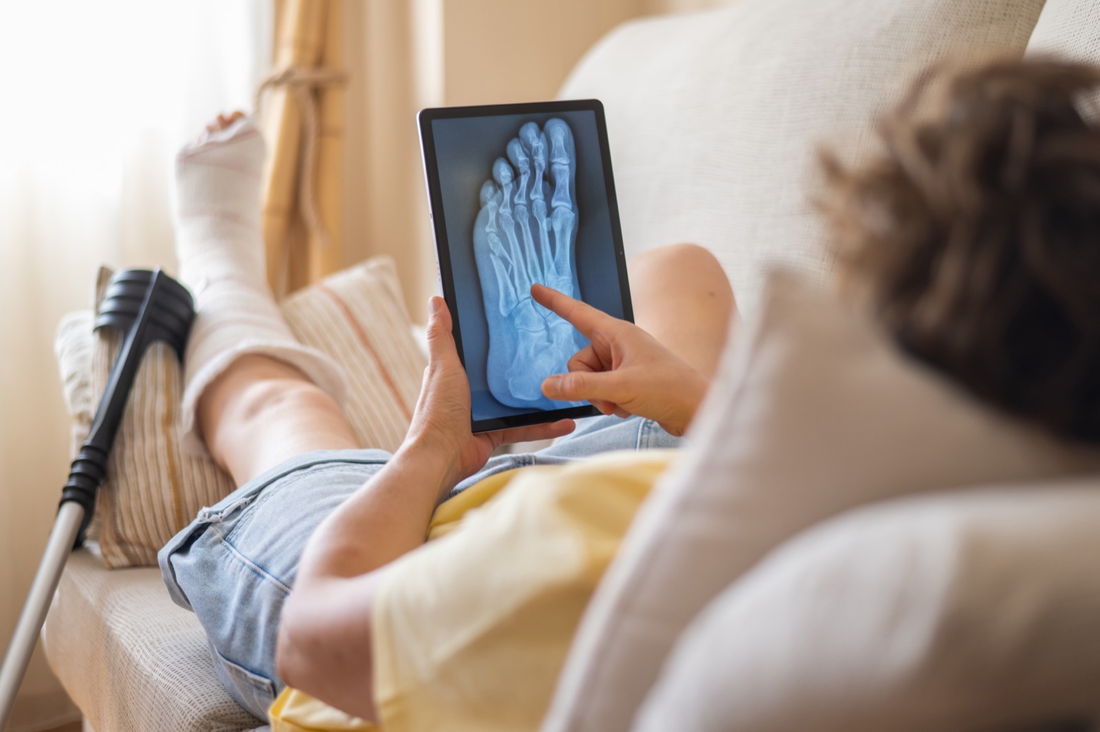 Patient at home reviewing a foot fracture X-ray on a tablet during an online fracture clinic consultation