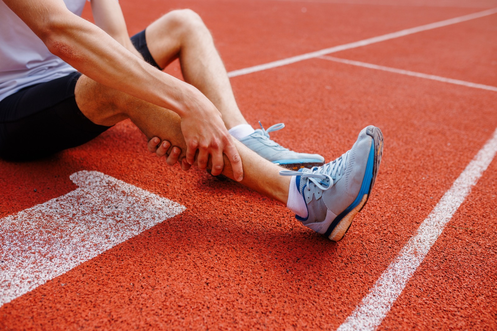 Runner holding an injured ankle on an athletics track