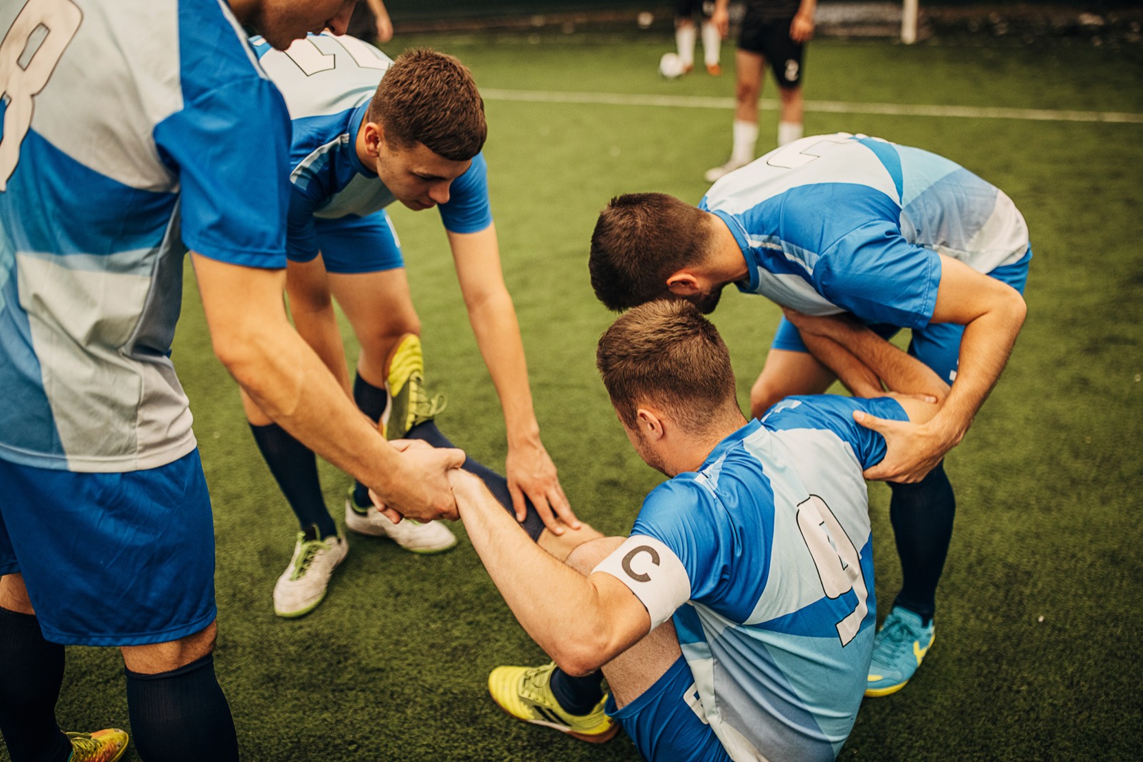 Teammates helping an injured football player off the pitch