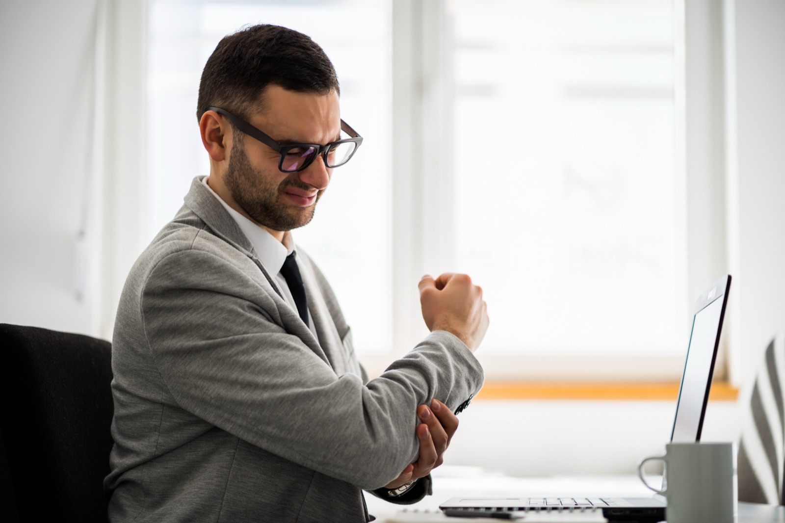 Man at his desk holding his elbow in pain, a candidate for a tennis elbow specialist assessment