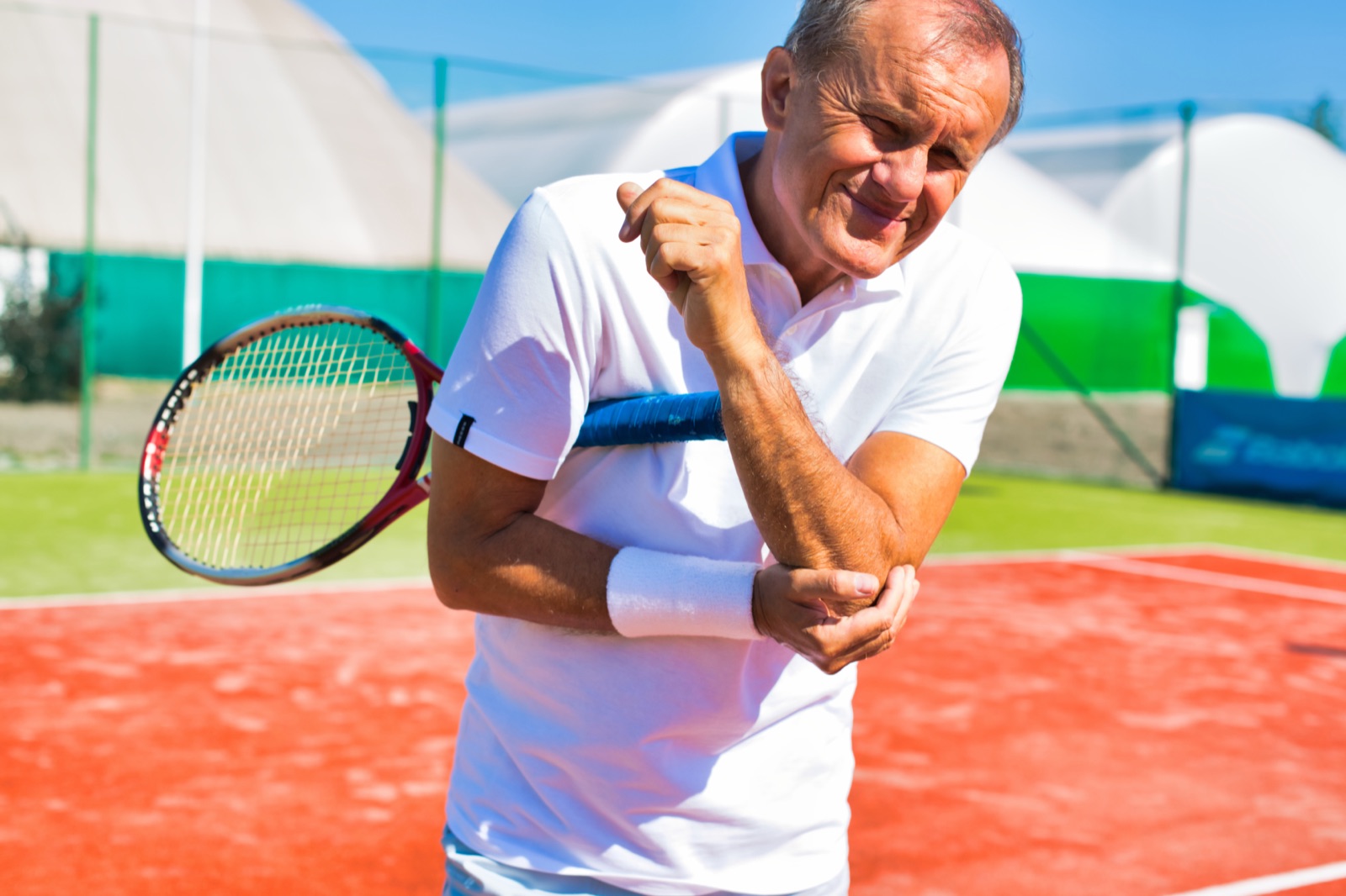 Senior man on a tennis court holding his elbow with tennis elbow symptoms